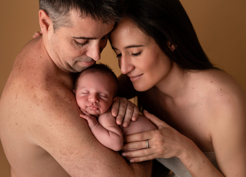 Padres con su bebé recién nacido en brazos en una foto familiar piel con piel