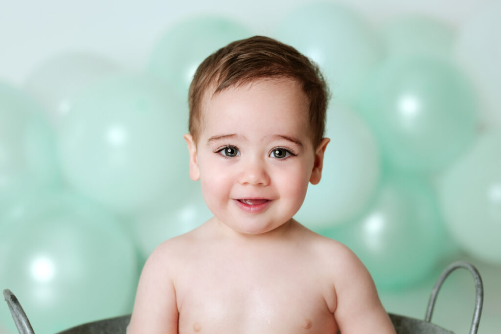Retrato de bebé sonriendo con globos verde menta de fondo en su primer cumpleaños