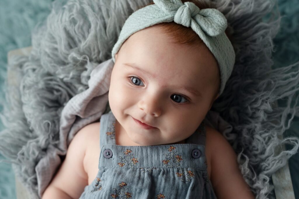 Bebé de cuatro meses tumbado sobre una manta de pelo con lazo verde, sonriendo a cámara