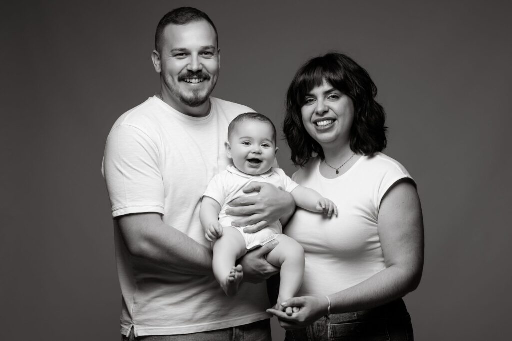 Papá y mamá sonriendo con su bebé en brazos en una sesión de fotos de bebé en blanco y negro