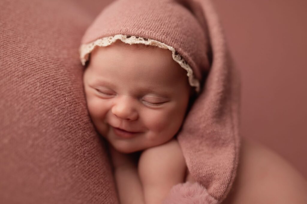 Bebé recién nacido sonriendo dormido con un gorrito rosa de encaje
