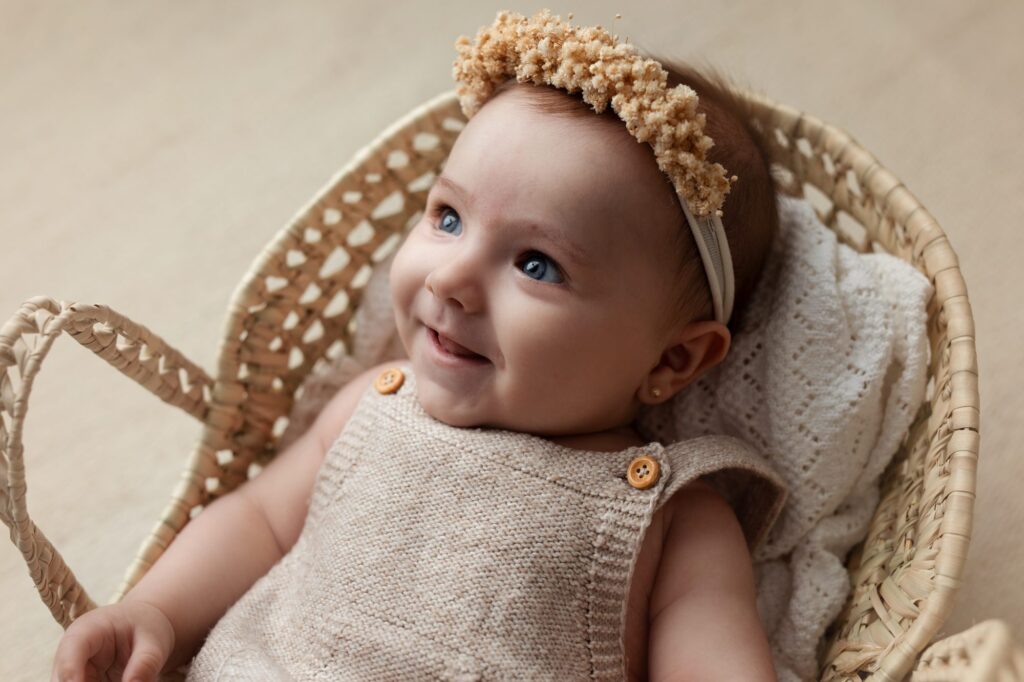 Bebé de cuatro meses sonriendo dentro de una cesta de mimbre con corona de flores secas