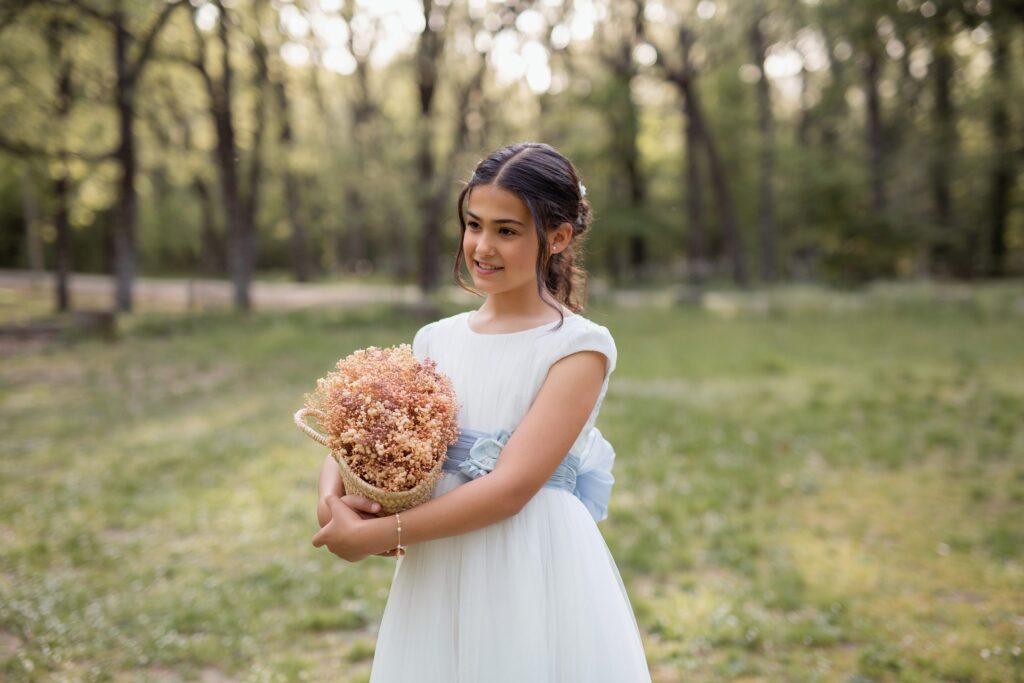 Niña con vestido de comunión sujetando una cestita con flores secas en el bosque