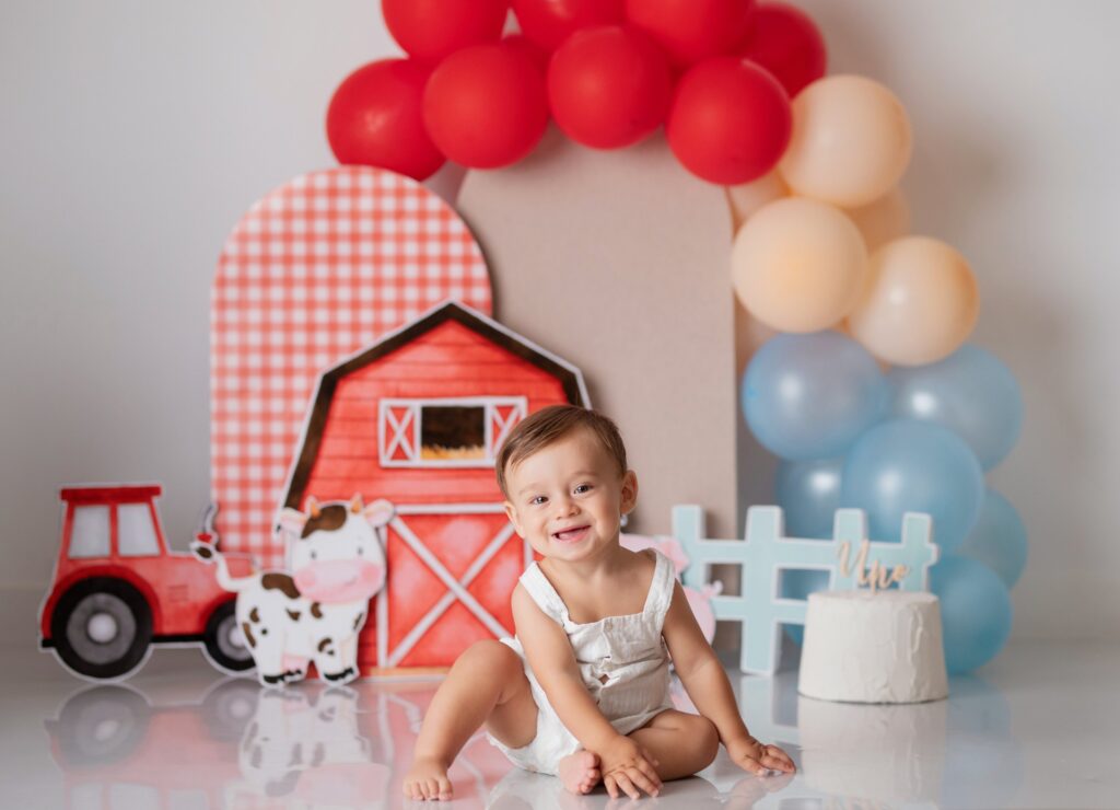 Niño sonriendo con su ropa en un escenario de granja con globos al empezar su sesión de cumpleaños