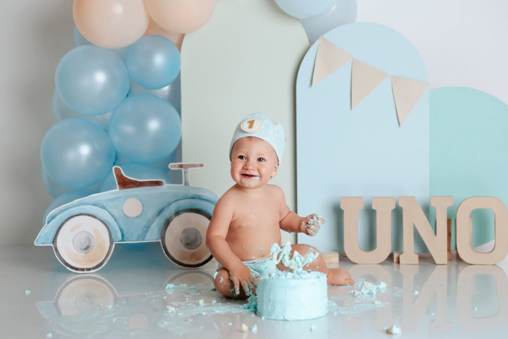 Bebé con corona riendo mientras destroza su tarta azul en una sesión smash cake de primer cumpleaños
